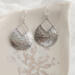 Close-up of sterling silver pear-shaped hammered dangle earrings with French hook ear wires on a marble surface.


